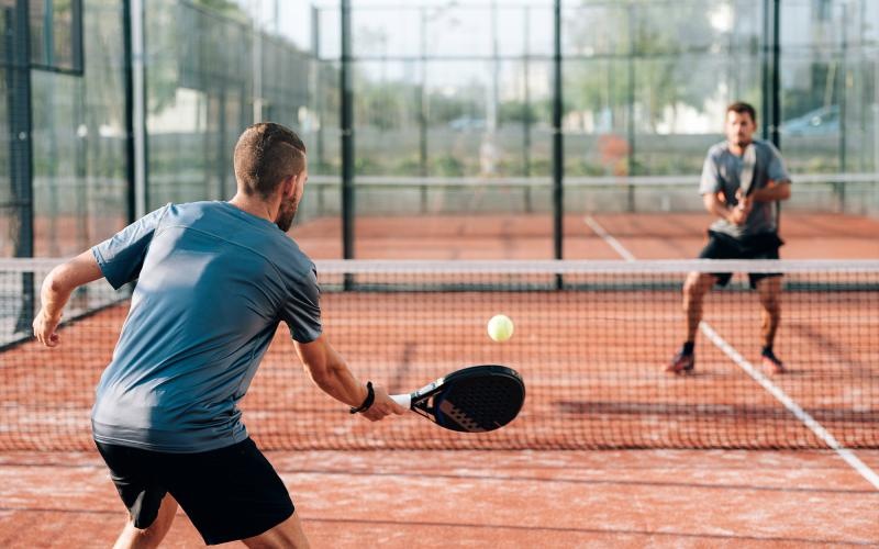 a person hitting a ball with a pickleball paddle to another person